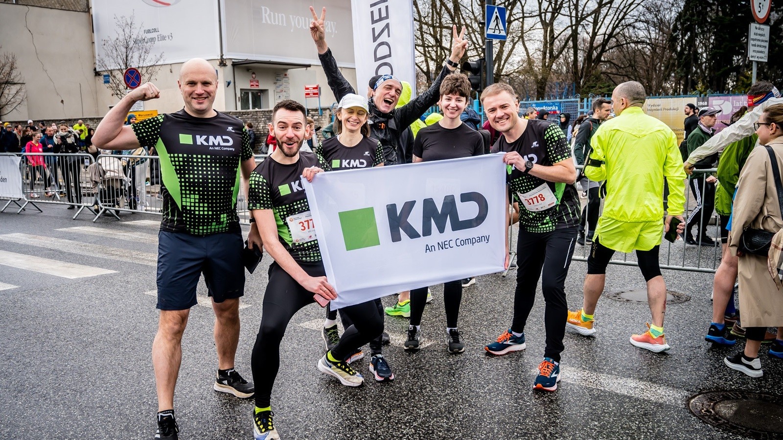 KMD Poland employees in sports attire holding up a KMD sign at a corporate running event