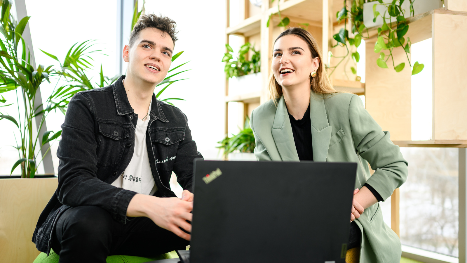 Man and woman looking up while sitting in a lounge in front of a laptop